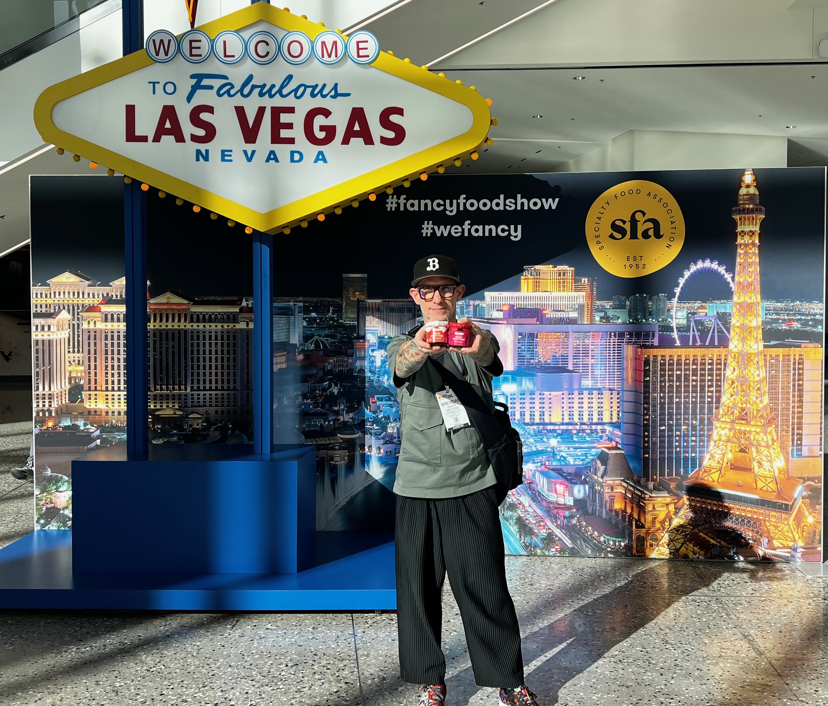 Brendan, founder of Azabu Foods, stands in front of a “Welcome to Fabulous Las Vegas” sign at the SFA’s Fancy Food Show 2025, holding a jar of Umami Everything. The backdrop features the Las Vegas skyline with the Specialty Food Association (SFA) logo and event hashtags. This marks the official U.S. launch of Umami Everything at one of the biggest food industry trade shows.